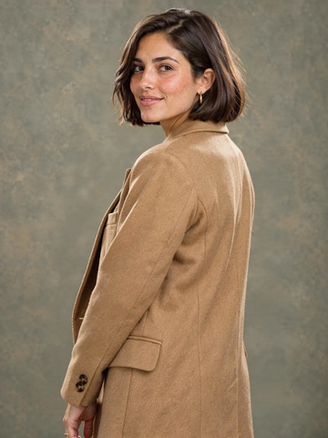 Magic Pose Changer sample: A head-on studio portrait turned into a look back over the shoulder, with the face, hair, earrings, blazer and backdrop held