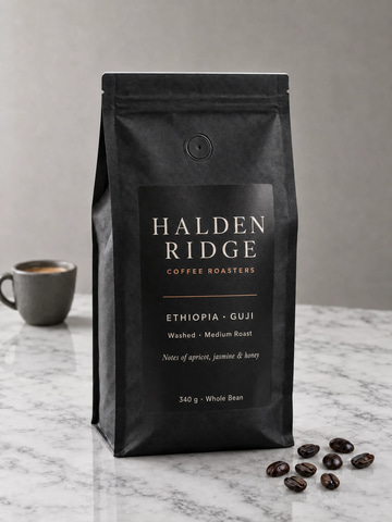 Precise Edit sample: A label reading HALDEN RIDGE COFFEE ROASTERS, Ethiopia Guji, typeset onto a blank black coffee pouch, with the pouch, marble, beans and light unchanged