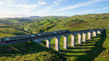 Join Clips sample: Joined edit: a train crosses a stone viaduct on a bright morning, then again at dusk.