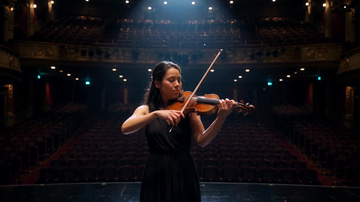 Imagera Warlord (Image) sample: A violinist plays alone on a theatre stage under one warm spotlight, the empty stalls behind her.
